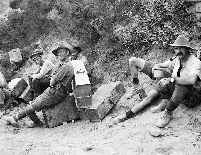Black and white photo of a handful of Australian soldiers resting on or near their suitcase-sized water containers