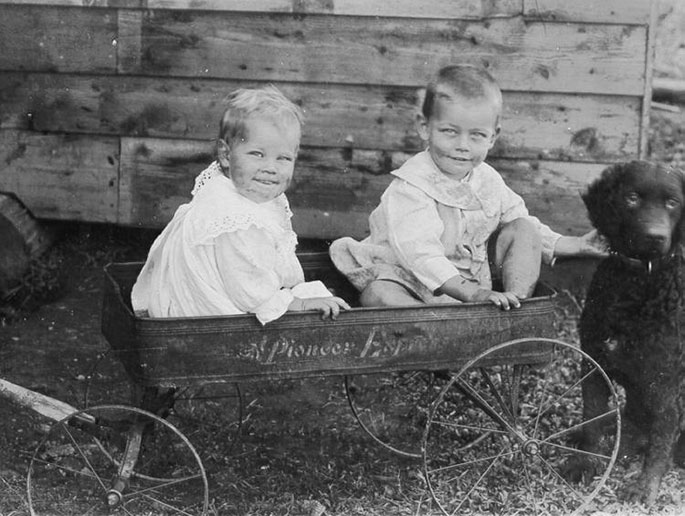 Two children under two smiling from inside a toy card. One is fondling a black puppy.