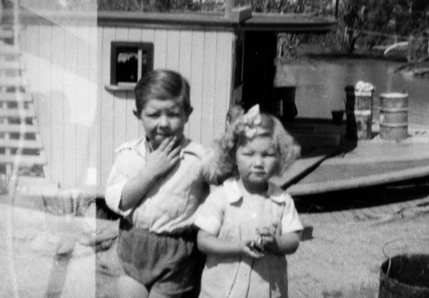 Black and white photo of a young boy and girl standing in front of a boat.
