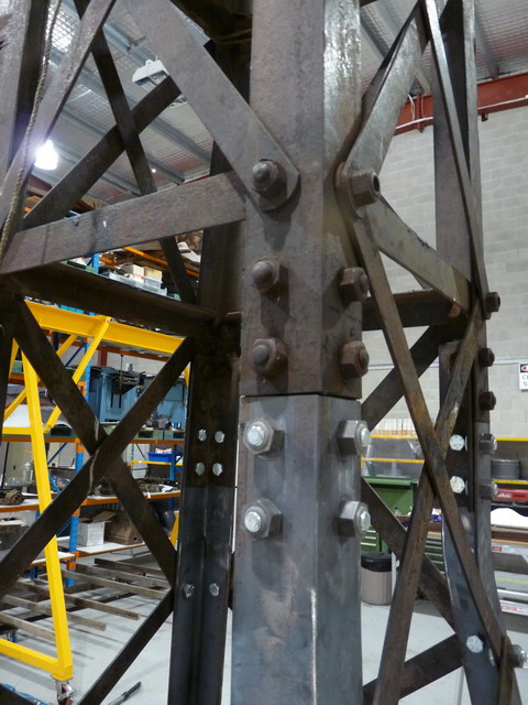 Detail of a windmill tower showing darker greyish steel section at the top, with cleaner, lighter grey steel section at the bottom.