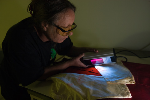 Conservator Deb Spoehr uses ultraviolet light to investigate staining on racing silks worn by the jockeys of Gaulus and the Grafter in 1897 and 1898 Melbourne Cup races.