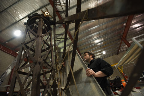 A man holds a piece of galvanised steel to a large metal windmill frame.