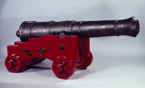 A cannon set on a replica wooden carriage constructed of unknown timbers with metal fittings painted red and black.