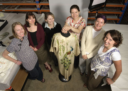 Six Accessions team members stand behind a pale yellow Japanese-style silk gown, with an embroidered peacock motif, displayed on a mannequin.