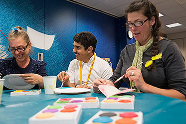 Three people at a table smiling as they paint paper plates