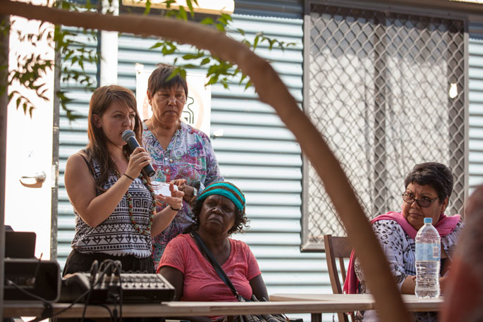 A women holding a microphone addresses an audience.