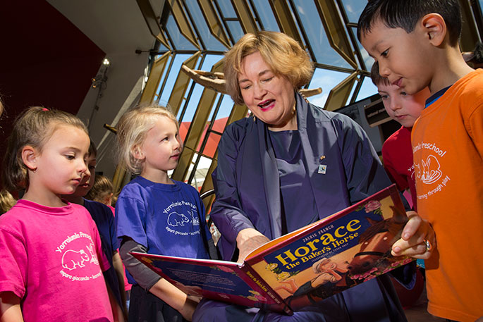Jackie French holding the book 'Horace the Baker's Horse' surrounded by children