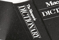 'Macquarie Dictionary' a black and white photo of four people inside an office. There is a bookcase behind them and the man seated is holding a Macquarie Dictionary