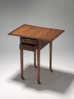 Rectangular wooden table, with fold-down side leaves. The table features narrow inlaid ivory borders, including a wide inlaid border of contrasting timber in a geometric pattern on the table top. The table has four square tapering wooden legs, each terminating in a brass cup and castor. The table has two drawers, each with two round metal knob handles and a brass key-operated lock.