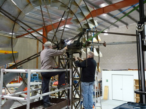 Rear view of two men working at height, on a windmill. One man is applying heat gun to a piece of metal.