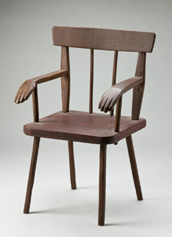 A wooden chair with decorative carved hands at the end of each arm.