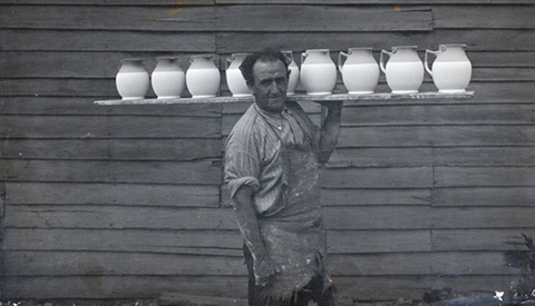 Photograph of Pottery employee H Dower carrying a board laden with jugs.