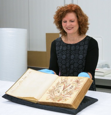 Woman with wavy red hair viewing an open book on a large table