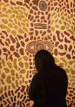 Rear view silhouette of a visitor looking at a dot painting.