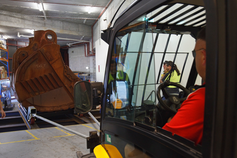 The forklift slowly reversing, towing the bucket off the temporary platform and into the gallery.