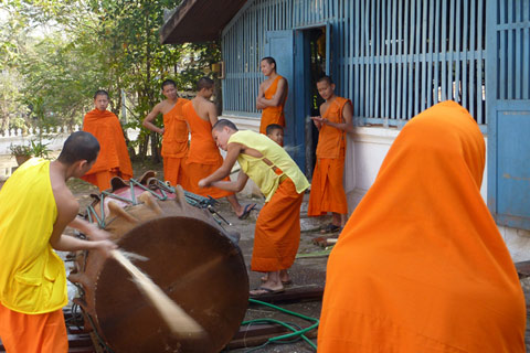 Ninne people dressed in orange and yellow fabric gather round a large cyclindrical drum.