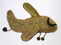 A sculpture depicting an aeroplane with its wheels down. The sculpture is made of woven grass, plant material dyed in different colours, wool and metallic thread.