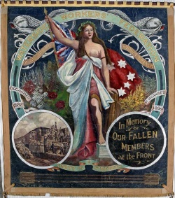 Large, almost square shaped banner painted in oil colours and showing a central image of a woman wearing loose flowing robes. She holds the red ensign and stands among native flowers. The text at the top reads 'Waterside Workers' Federation of Australia, Sydney branch'. An inset image at the bottom left shows workers handling numerous sacks and an inset at the bottom right reads 'In Memory of OUR FALLEN MEMBERS at the Front'. The motto 'Unity is Strength' joins the two insets.