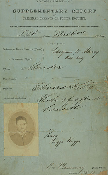 A stained form completed in copperplate handwriting. Under the heading ‘Offence’ the word ‘Murder’ has been written. A photo of Ned Kelly appears bottom left.