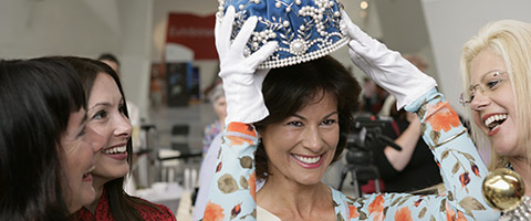 Lea Dickson, with her hands in white gloves, holding the Miss Australia crown above her head, watched by three other former titleholders.