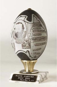 The egg, carved by craftsman Peter Harris, depicts a map of the journey of Burke and Wills. The egg rests on a marble base with a gold-plated plaque. The engraved text reads 'HAND CARVED / EMU EGG / Peter J. Harris GL 470'.