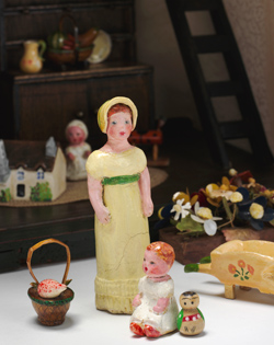 Miniature figures of a young woman and a baby, a basket and flower cart.