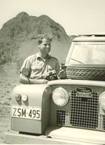 Black and white image showing Bob Edwards standing beside a Landrover, with a rocky formation in the background.