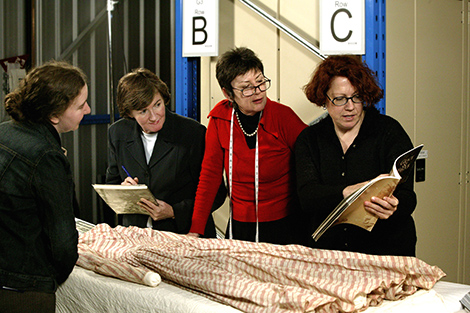 Four women looking at pink and white striped dress and book.