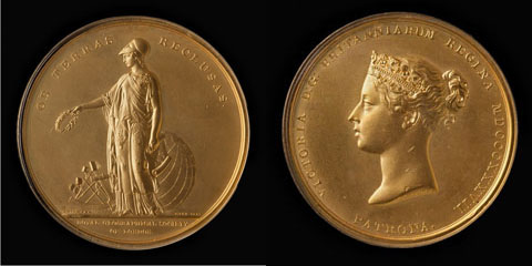 Image showing two sides of a gold medal on a black backdrop. The face on the left shows a figure of a woman with a laurel wreath in her right arm and a map in her left, with a sextant and globe behind her. The face on the right shows the profile of a woman wearing a crown.