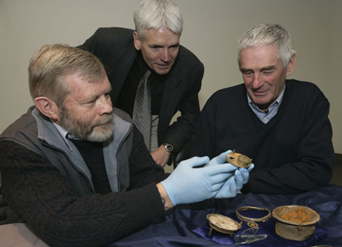 Three men examine rusted remants of a clock.