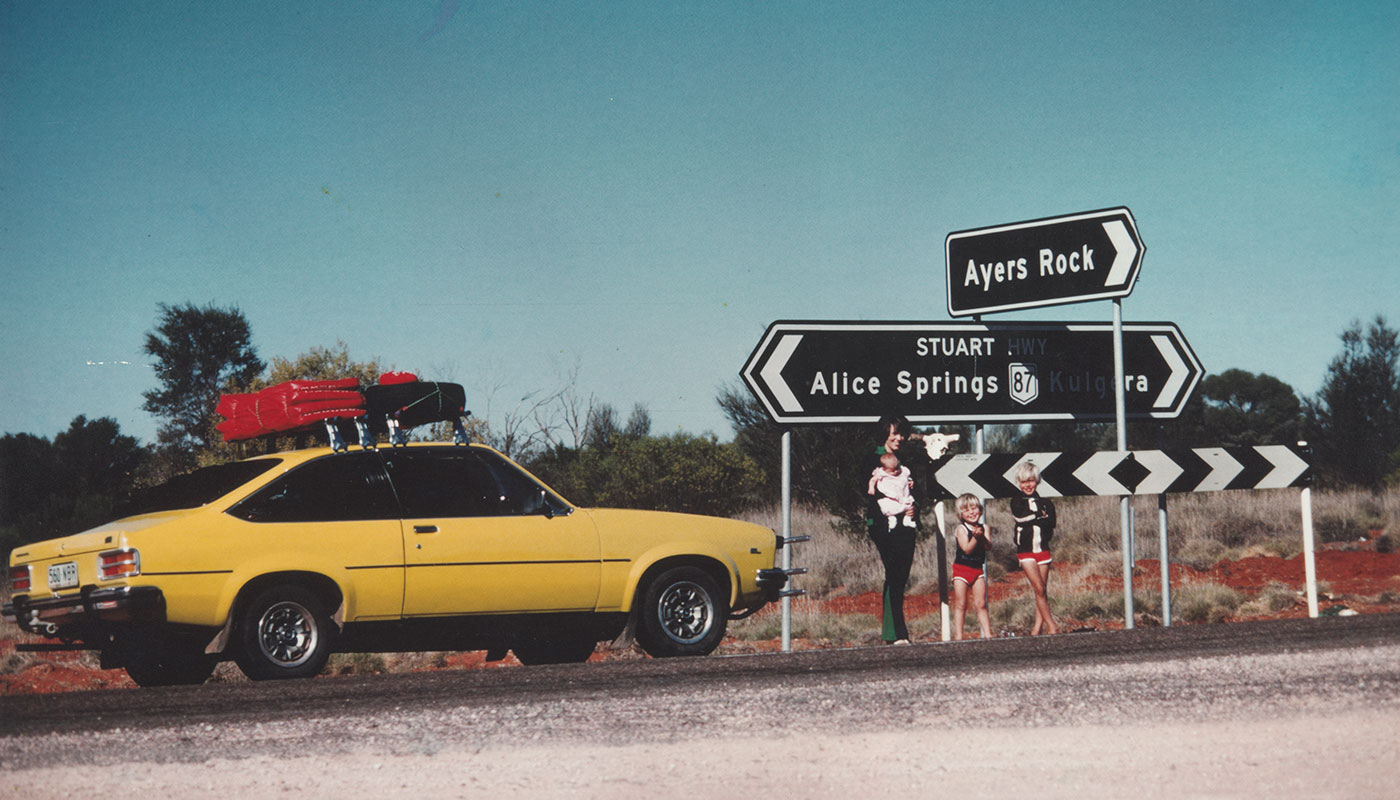 Lindy Chamberlain holding Azaria Chamberlain, with Aidan and Reagan Chamberlain, standing on Stuart Highway with sign to 'Ayers Rock', alongside their Torana, 16 August, 1980.