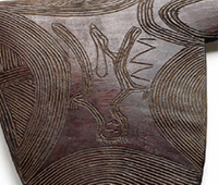 Detail showing rounded striking section of a wooden club. Concentric lines have been engraved on the edges and a human form is visible at the centre.
