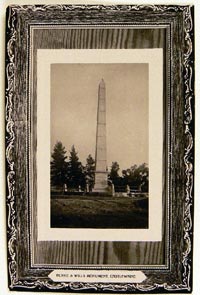 An unused postcard featuring a slightly pressed black and white photograph of a stone or concrete obelisk with a fence around it. The text reads 'BURKE AND WILLS MONUMENT, CASTLEMAINE'.