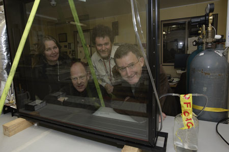 Conservation team members peer through the new glass case, with gas cylinder off to the side, in the laboratory