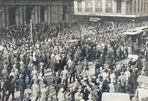 Black and white photograph showing a crowd of people in a city street.