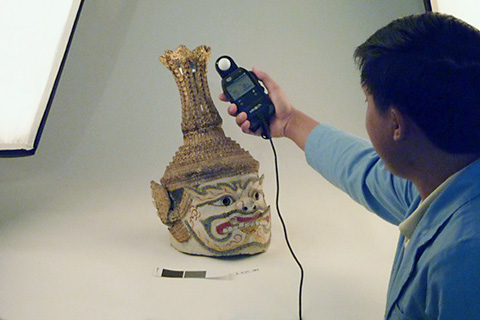 A man on the right leans into the photo, holding a small electronic device above an ornate headdress.