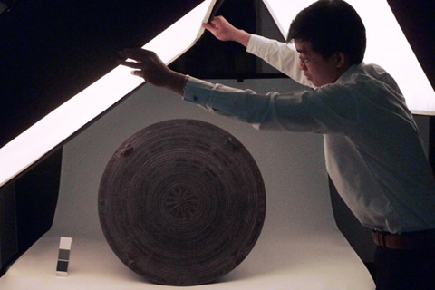 Mr Phoxay Inkong, Assistant Research and Exhibitions, moves lighting into position for detailed photography of musical drum.