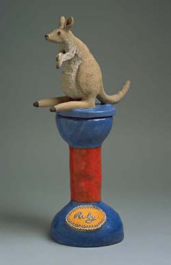Ceramic kangaroo figure mounted on the lid of a box, in the form of a red column with a blue base. 'Ruby' is written on a yellow oval medallion applied to the side of the plinth.