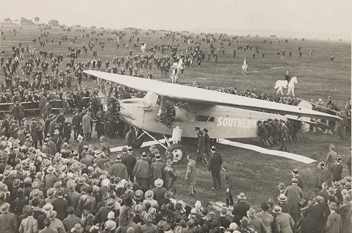 An aeroplane on the ground surrounded by a large crowd of people.