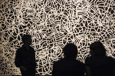 Silhouetted view of three people looking at a large black and white painting, 'Big Yam Dreaming' (1995), by Emily Kame Kngwarreye.