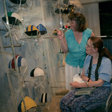 Two women, one in a wheelchair, inspect the display of surf lifesaving caps on display in the Between the Flags exhibition.