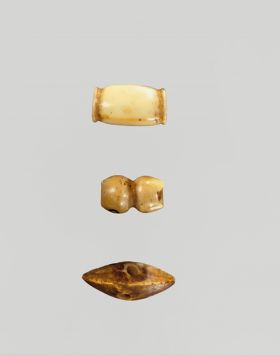 Three bone ornaments. The first is barrel-shaped, the second is a round long piece grooved around the middle, and the third is in the shape of a boat or roof.