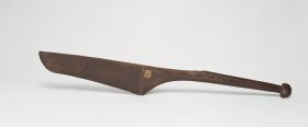 Dance paddle made of wood with an almost rectangular and rounded blade (that is damaged on one side) and a semi-circular knob at the end of the handle.