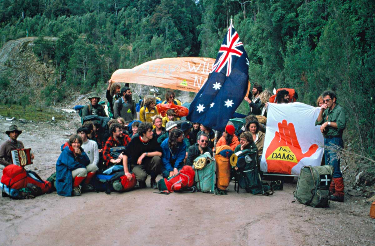 Young people squatting or standing on a dirt road holding the Australian flag and various banners.
