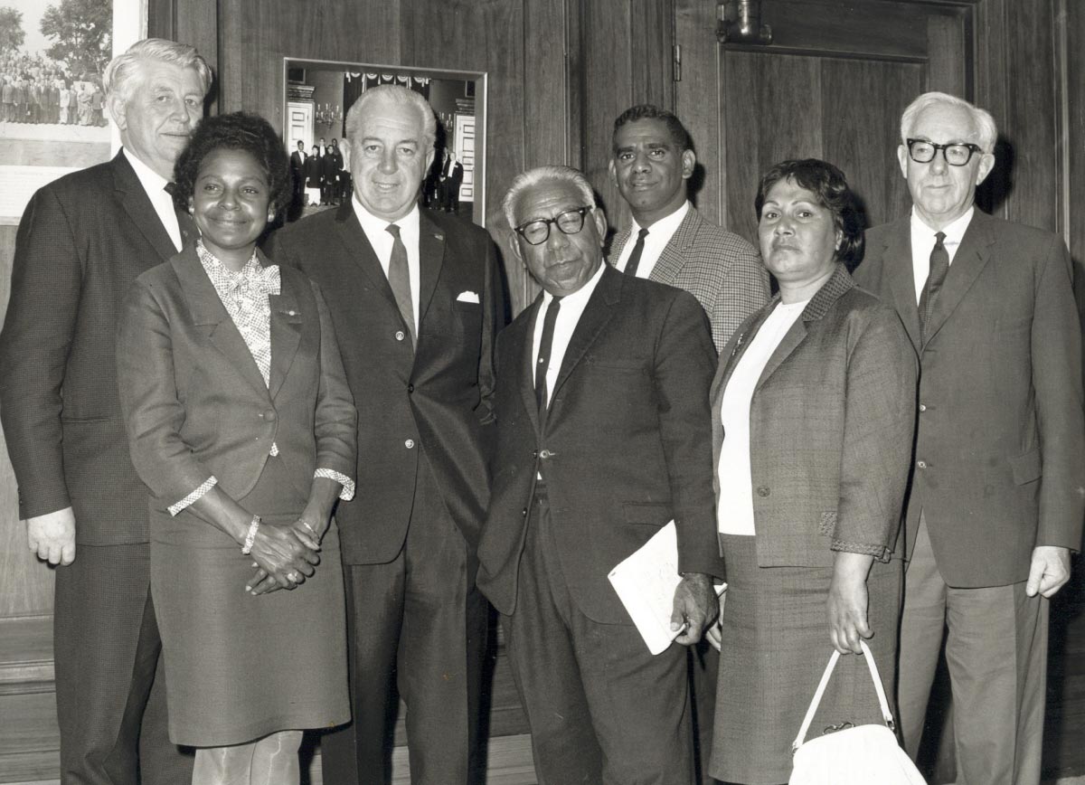 The seven people named stand in front of a wood-panelled wall in what looks like Old Parliament House.