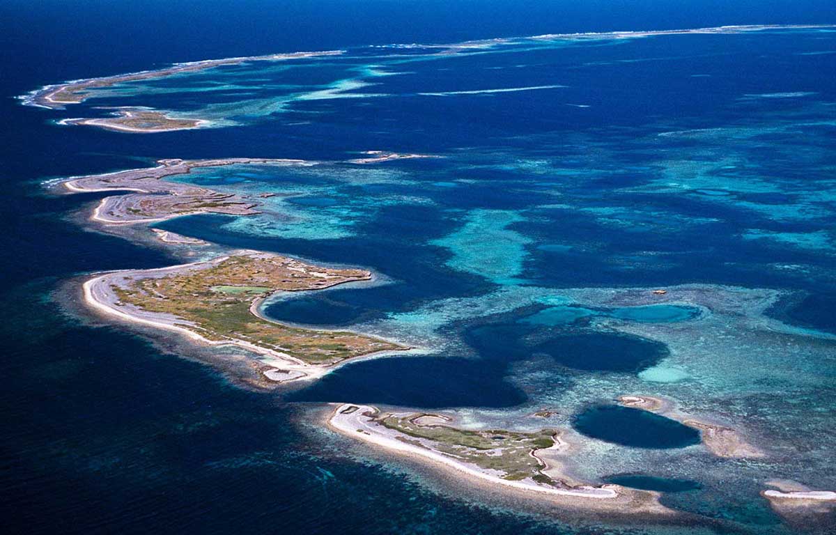 Aerial shot of five islets surrounded by reefs and deeper sea.