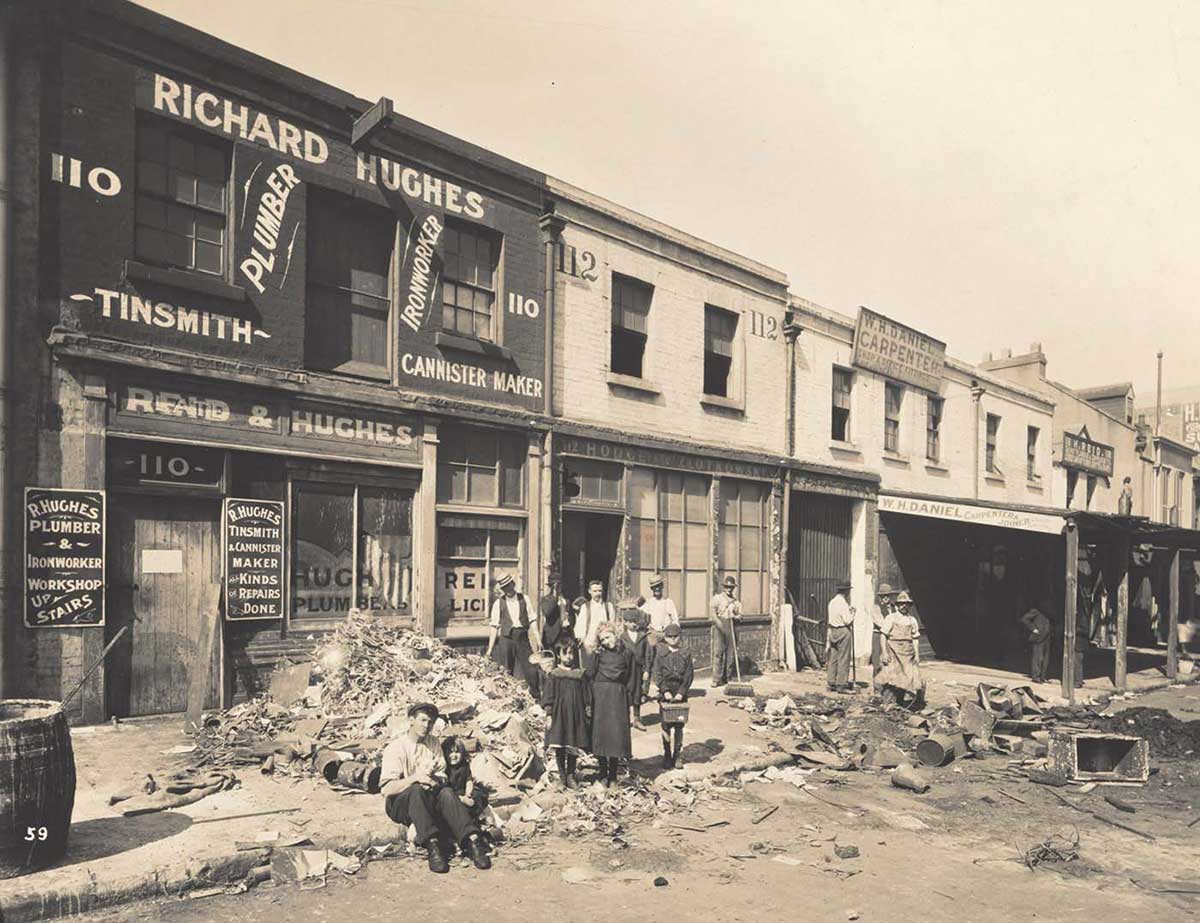 A dozen or so people pose in front of shop fronts amid rubbish that has been removed from the interiors of buildings.