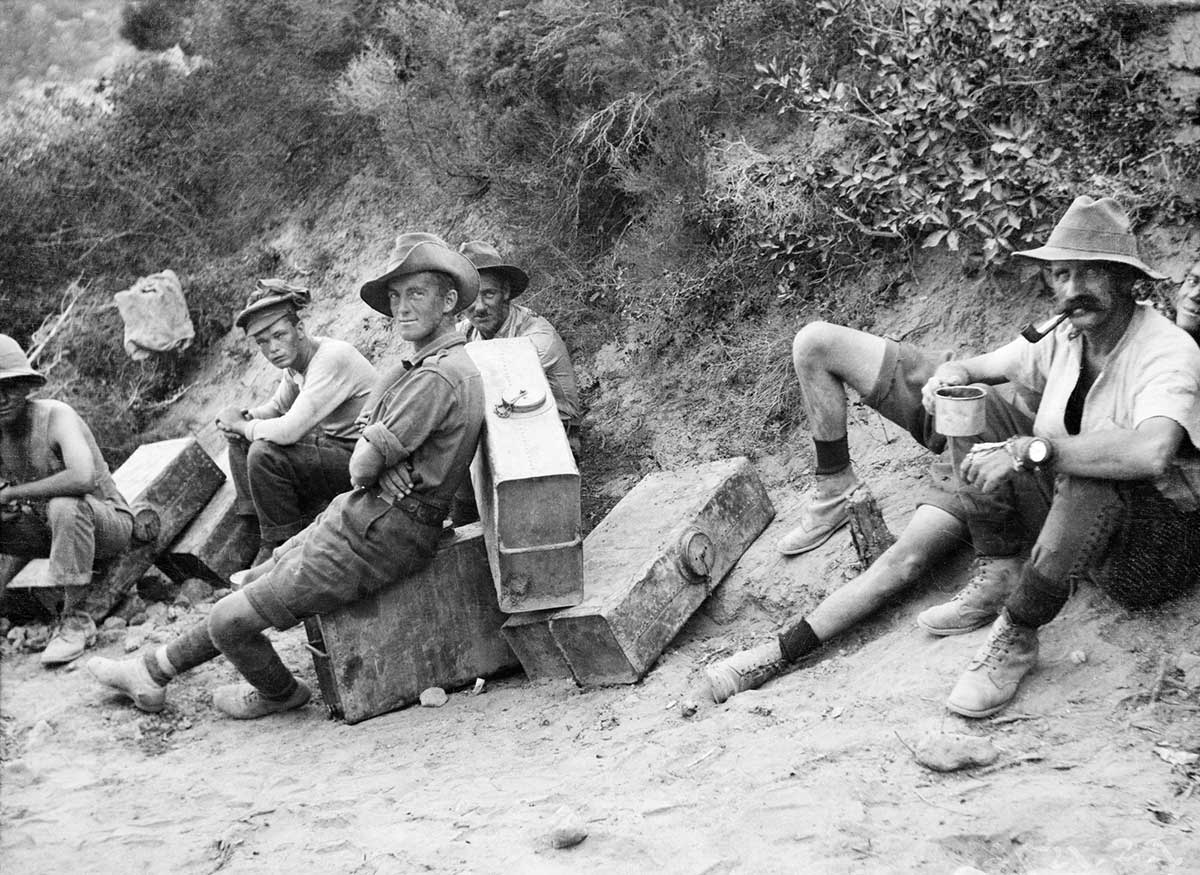 Black and white photo of a handful of Australian soldiers resting on or near their suitcase-sized water containers