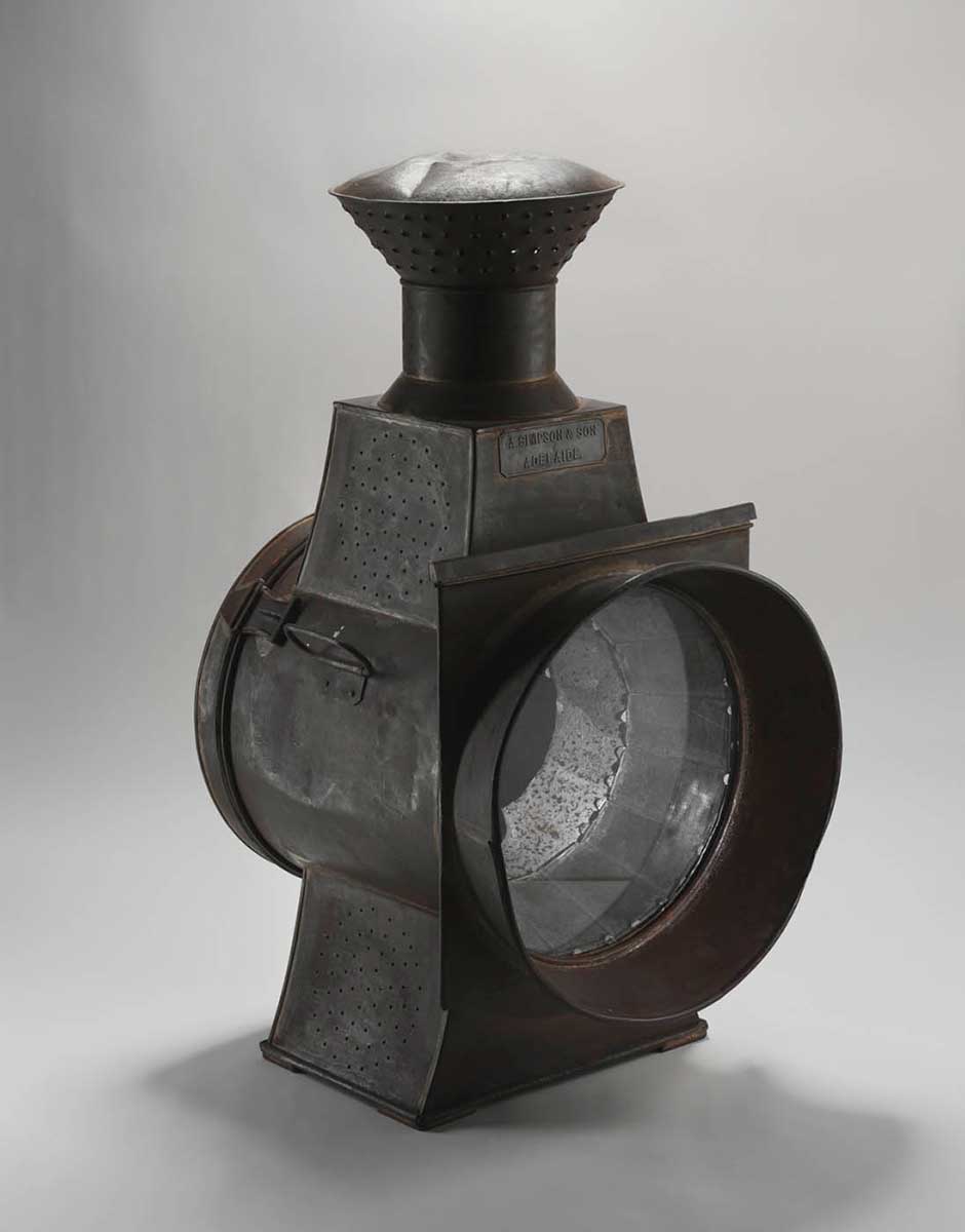 Black-coloured lamp with light metallic casing and circular glass panel at the front. - click to view larger image