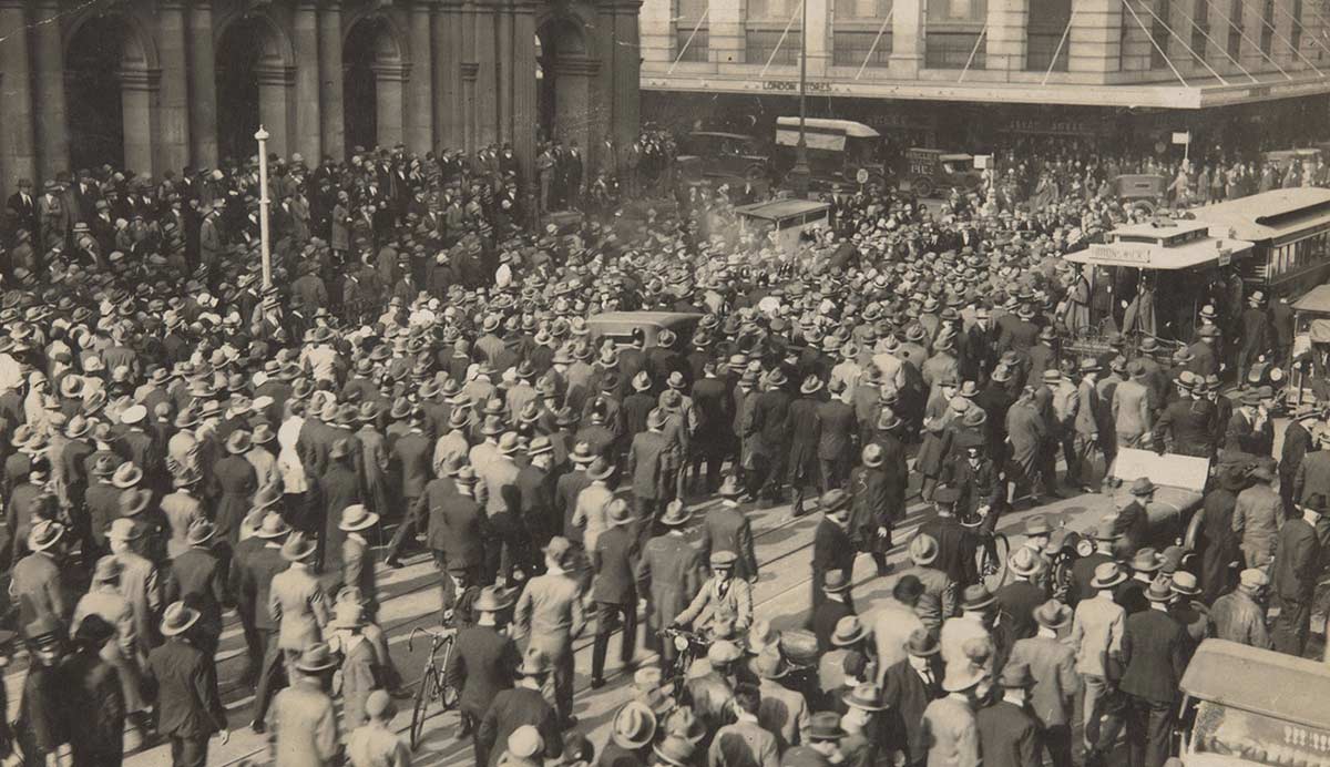 Black and white photograph showing a crowd of people in a city street.
